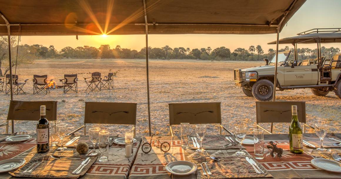 Letaka camp dining table at sunset with campfire and Land Cruiser
